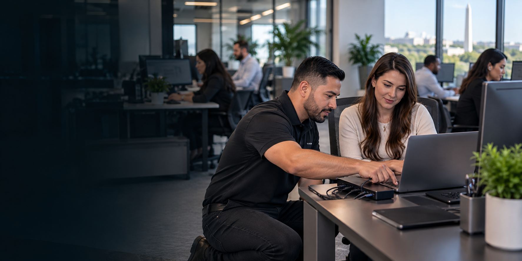 Illustrative IT technician helping a staff member with a laptop setup in a bright office overlooking Washington DC